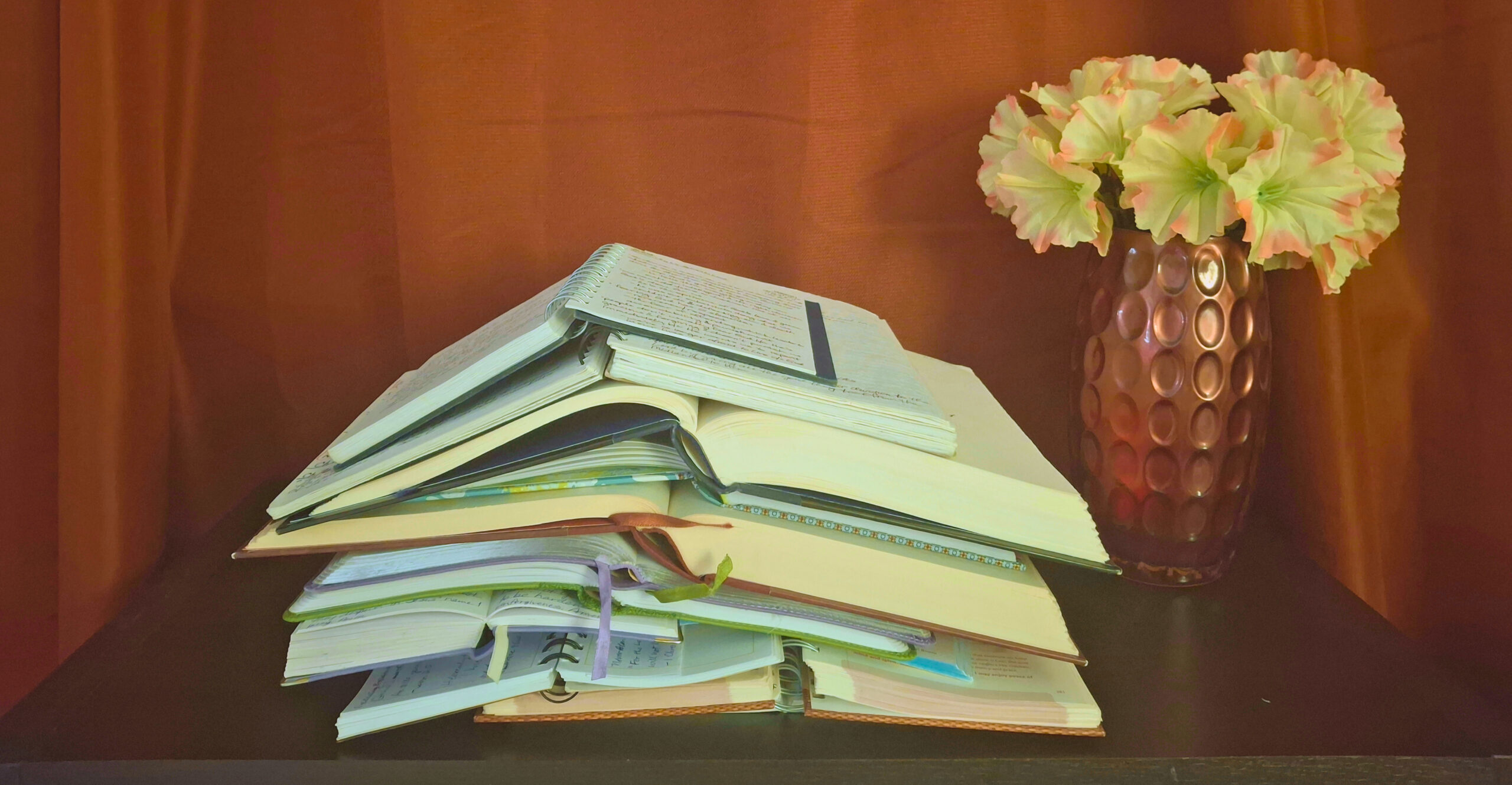 Stack of open journals on a table next to a flower vase