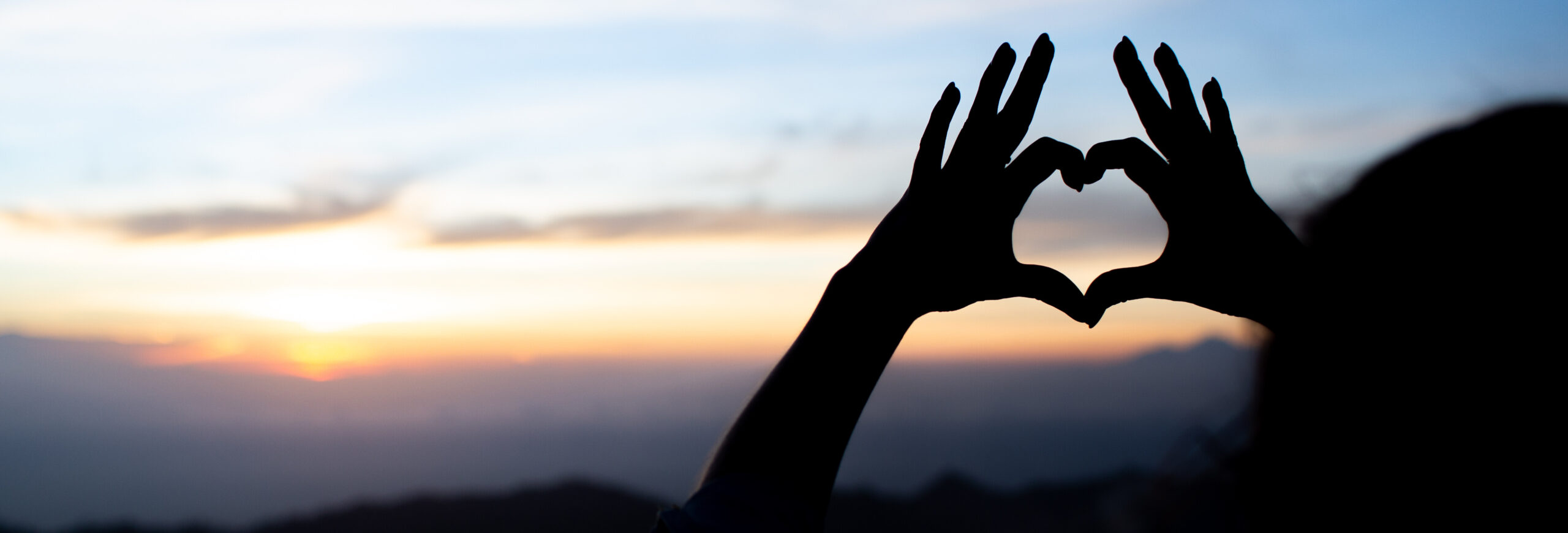 Hands in heart shape with sunset in background