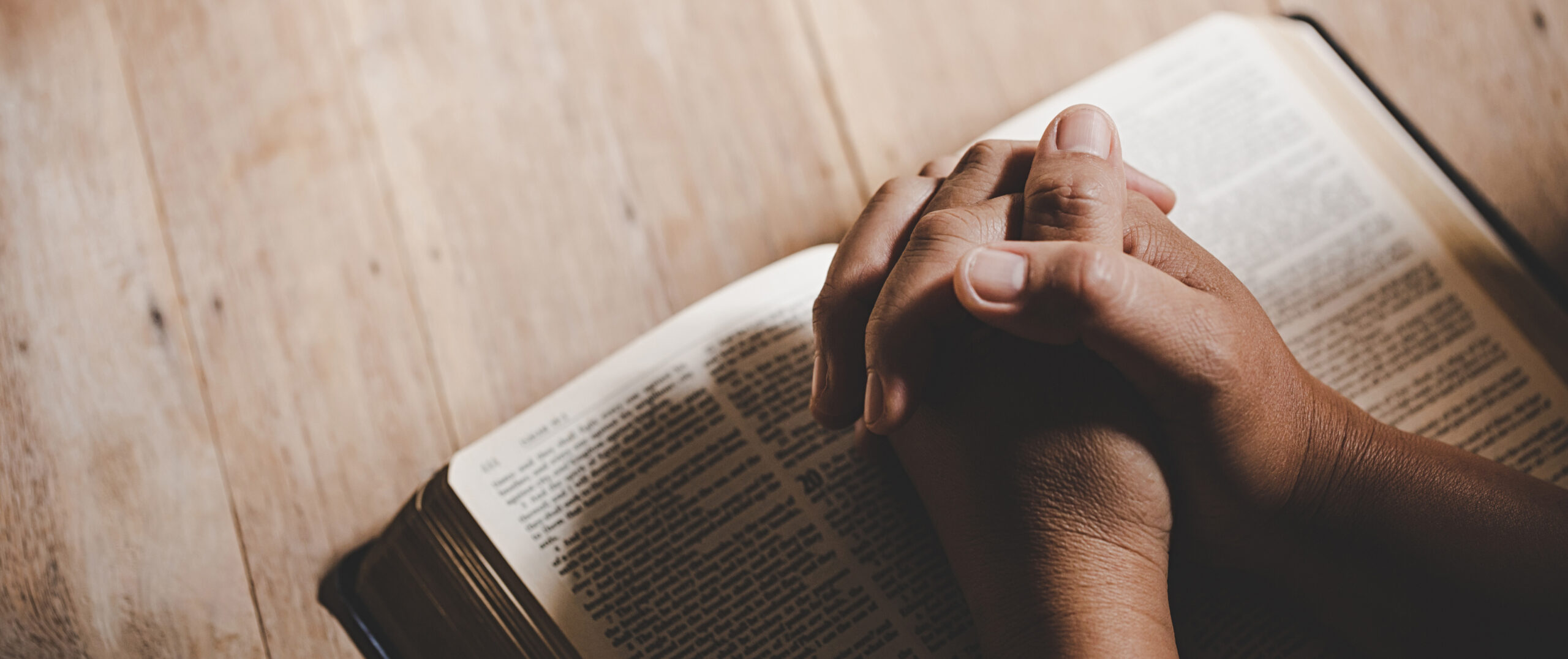 Folded praying hands on a Bible