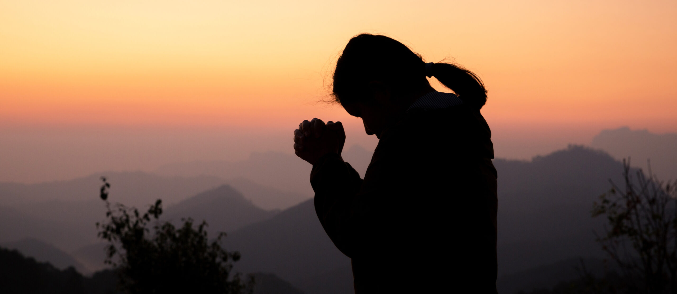 Silhouette of woman praying with sunset in background