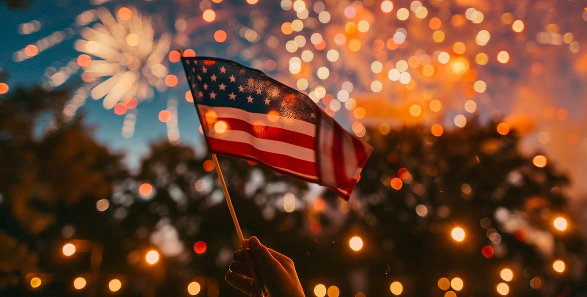 Hand holding American flag with fireworks in background