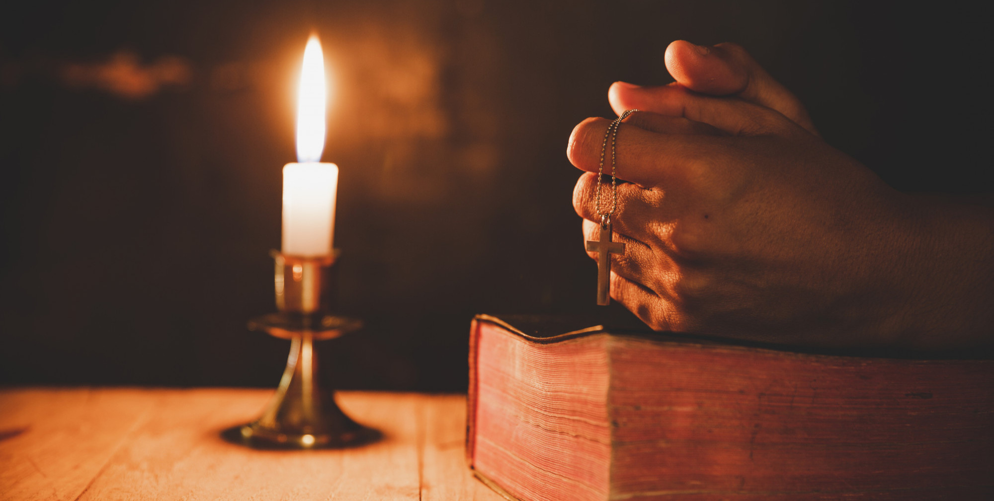 Praying hands holding cross on a Bible